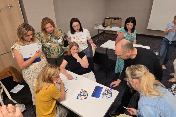 Uczestnicy siedzą przy stole i układają patyczki.