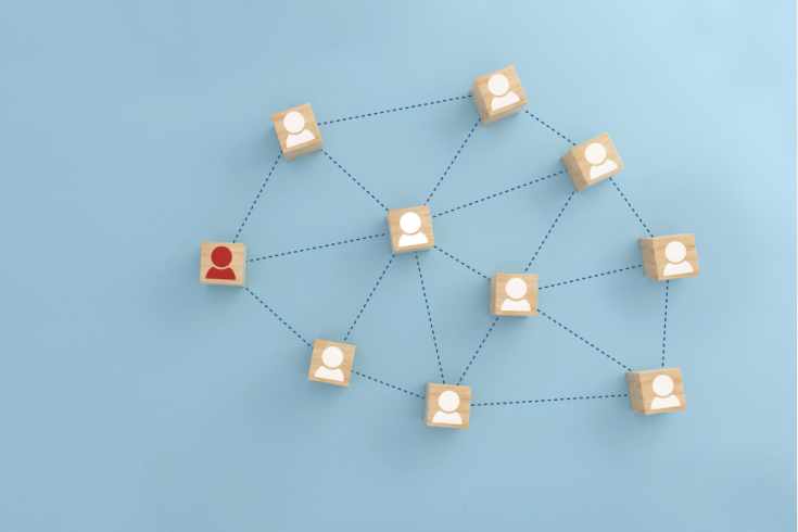 Drewniane kostki z białymi ikonami profili połączone przerywanymi liniami tworzą sieć relacji; jedna kostka z czerwoną ikoną wyróżnia się na tle pozostałych.